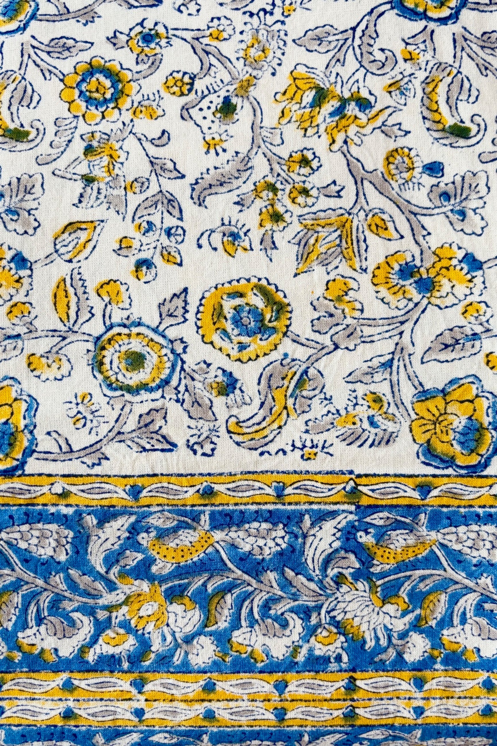 Detail of Hand printed, 100% cotton, Provence tablecloth with yellow and blue floral pattern draped on a table against a white wall 