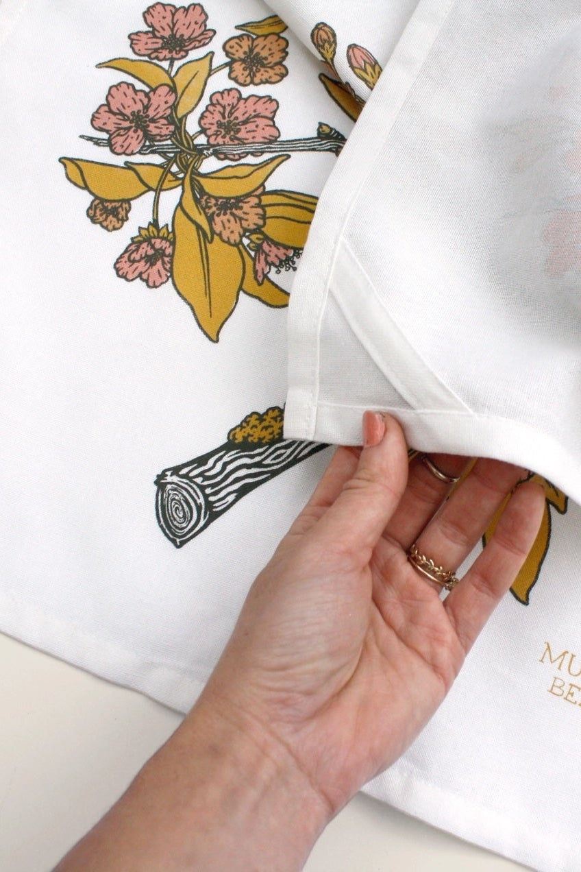 A pink and yellow screenprint of birds on branches on a white cotton tea towel ©Mustard Beetle