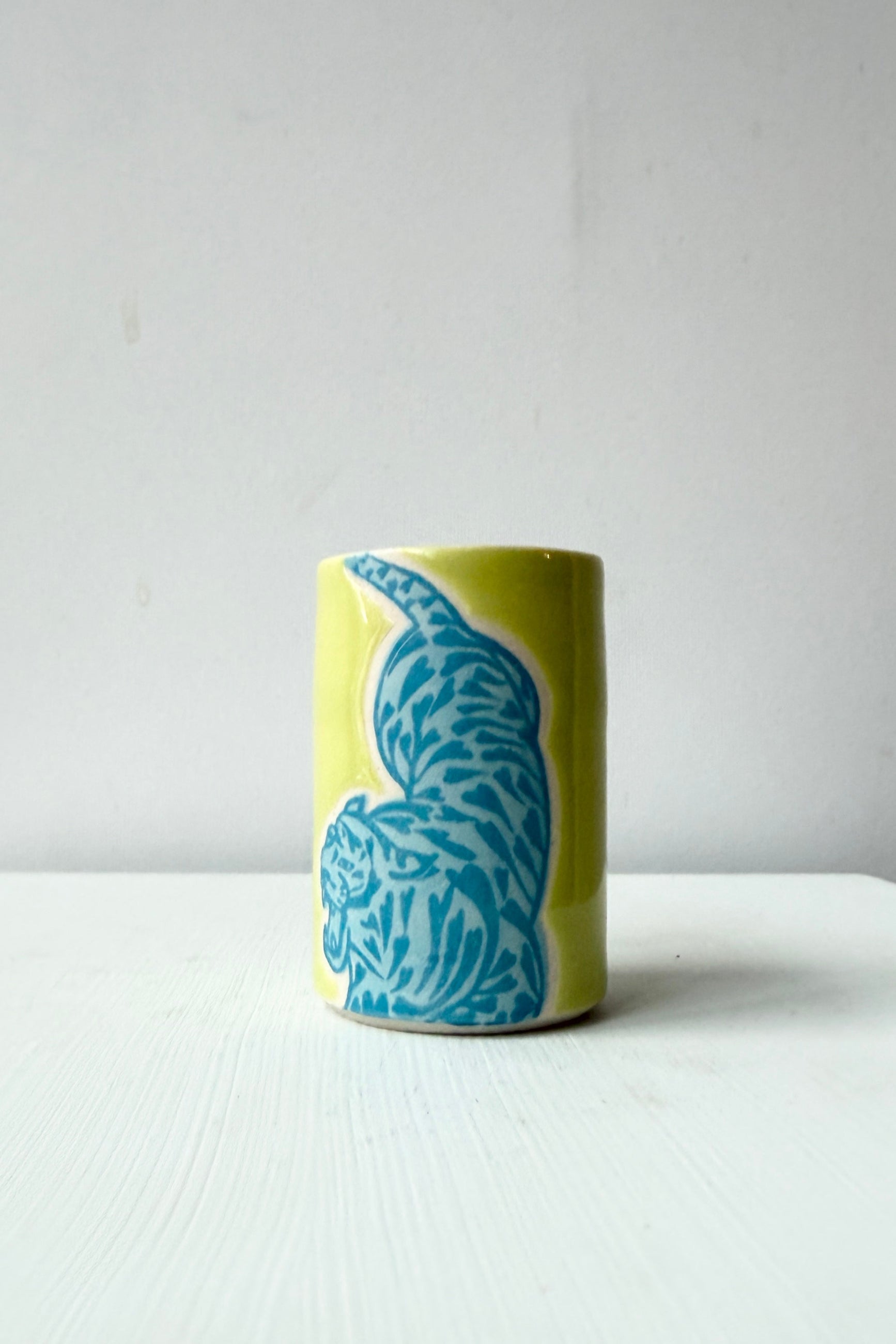 Yellow mug with blue tiger design hand made by City in Bloom Ceramics n a white surface and light gray background ©Sprout Home