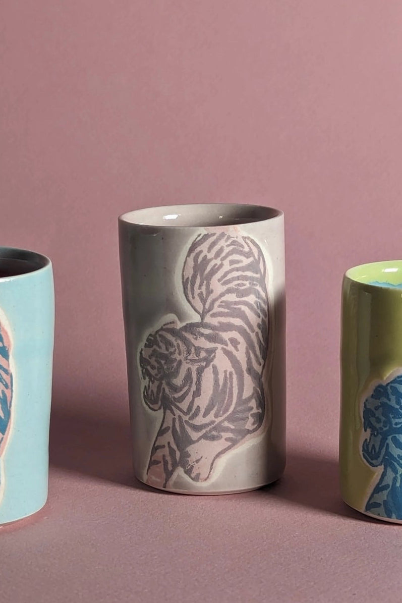 Ceramic cups with animal patterns on a pink background focusing on the mauve colored one in the center ©City in Bloom Ceramics
