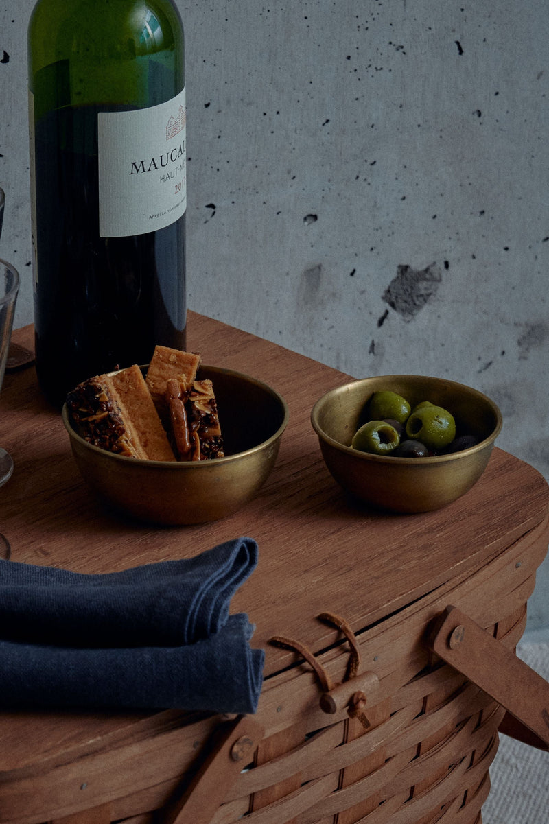 Brass bowls by Fog Linen Work in a lifestyle shot on top of a wood picnic basket with a bottle of wine. 