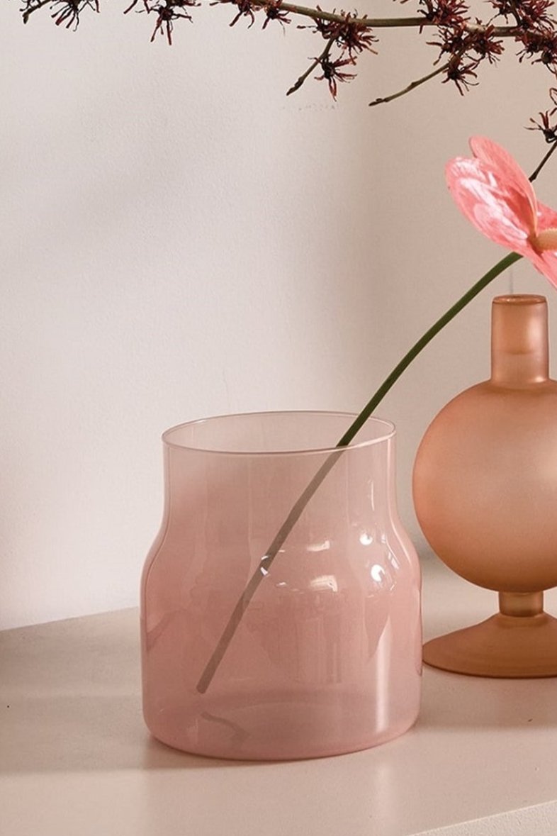 The Bodii Vase with a pink anthurium inside and another smoked pink vase next to it on a shelf.