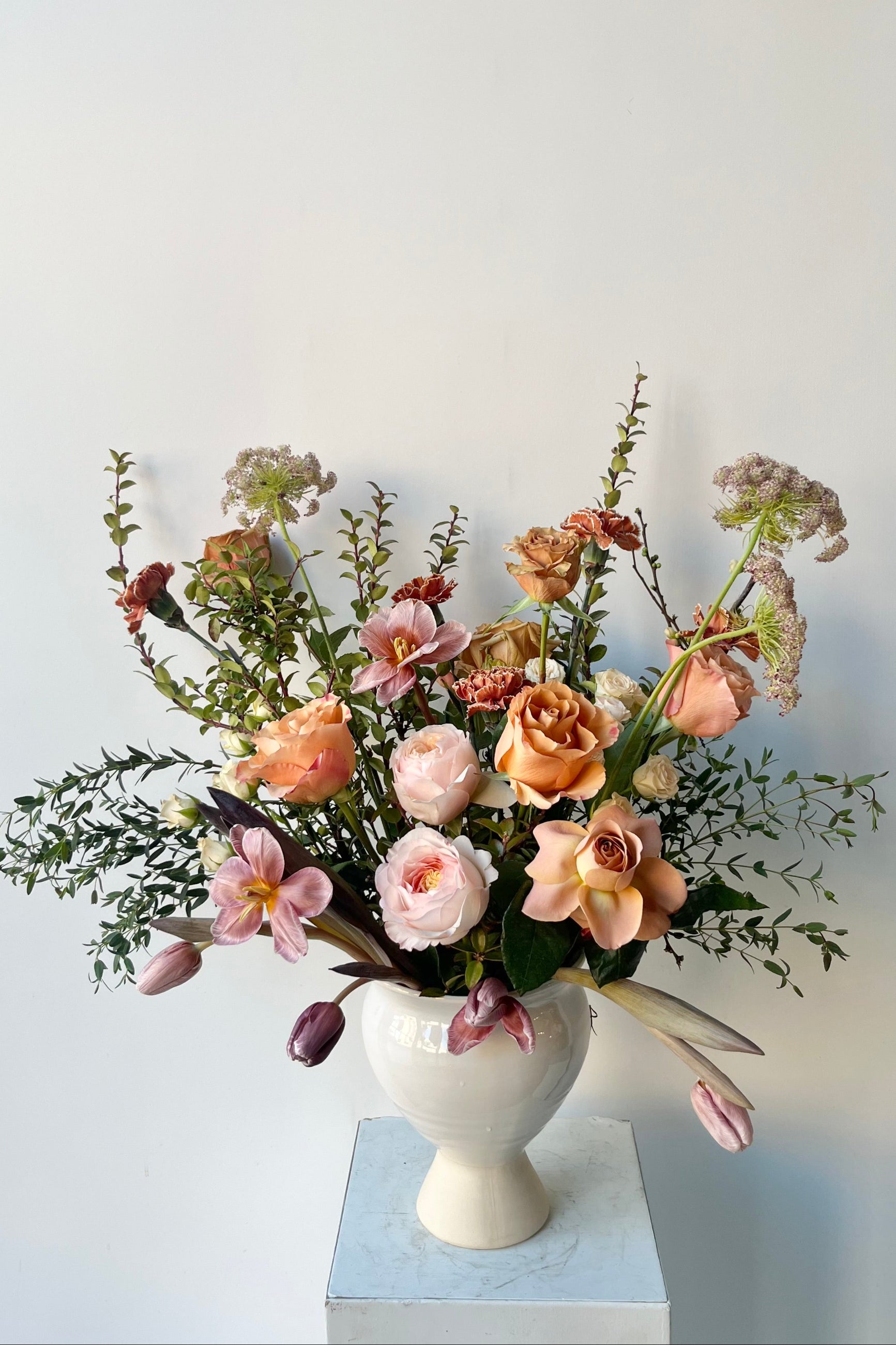 A Sprout Home floral arrangement in a white urn with dyed tulips and roses with warm neutral colors in late winter ©Sprout Home #size_$200