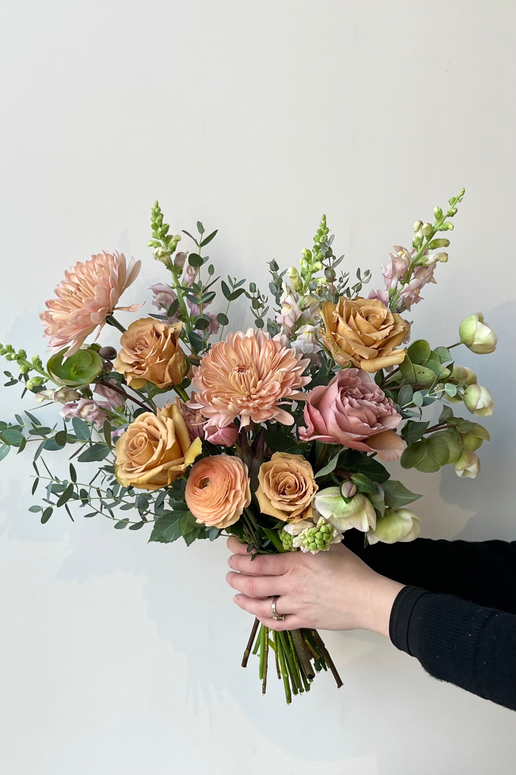 A Sprout Home floral arrangement held in front of a white wall with warmly neutral roses and ranunculus ©Sprout Home #size_$130