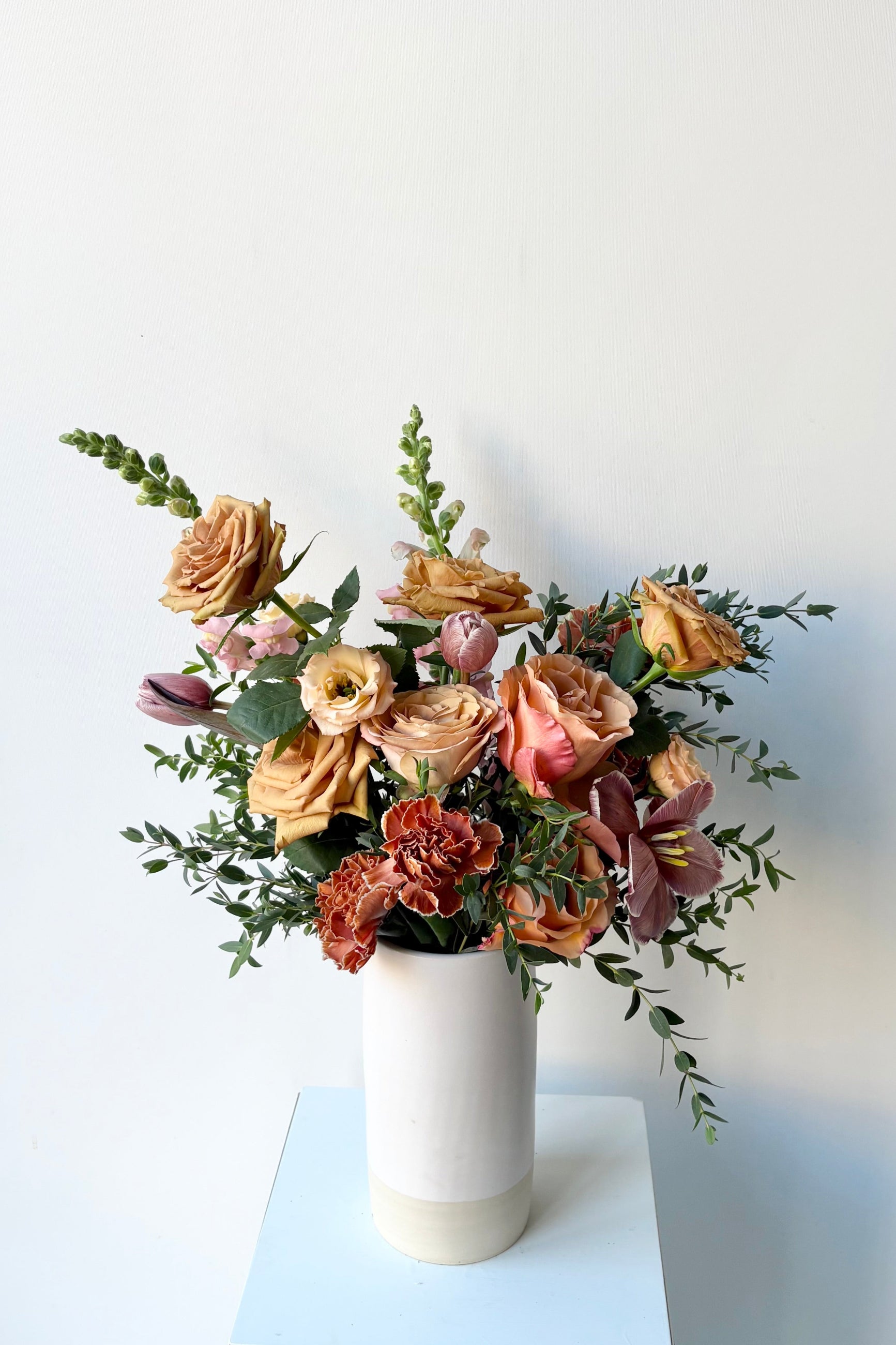 A bouquet in a white vase with caramel and bronze colors roses and dyed dianthus in late winter ©Sprout Home #size_$100