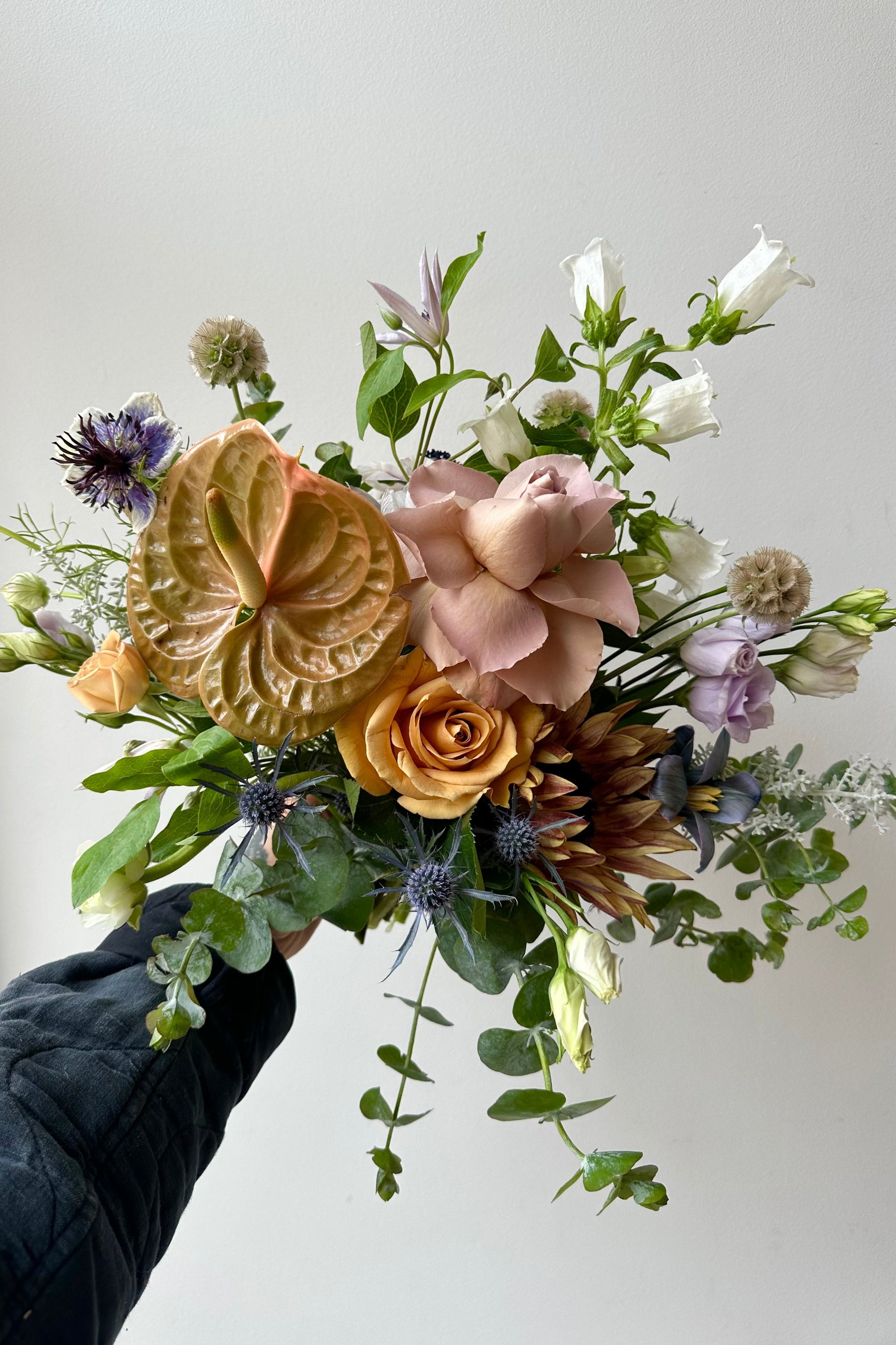A bouquet held in front of a white wall with caramel and bronze colors roses and dyed dianthus in late winter ©Sprout Home #size_$100