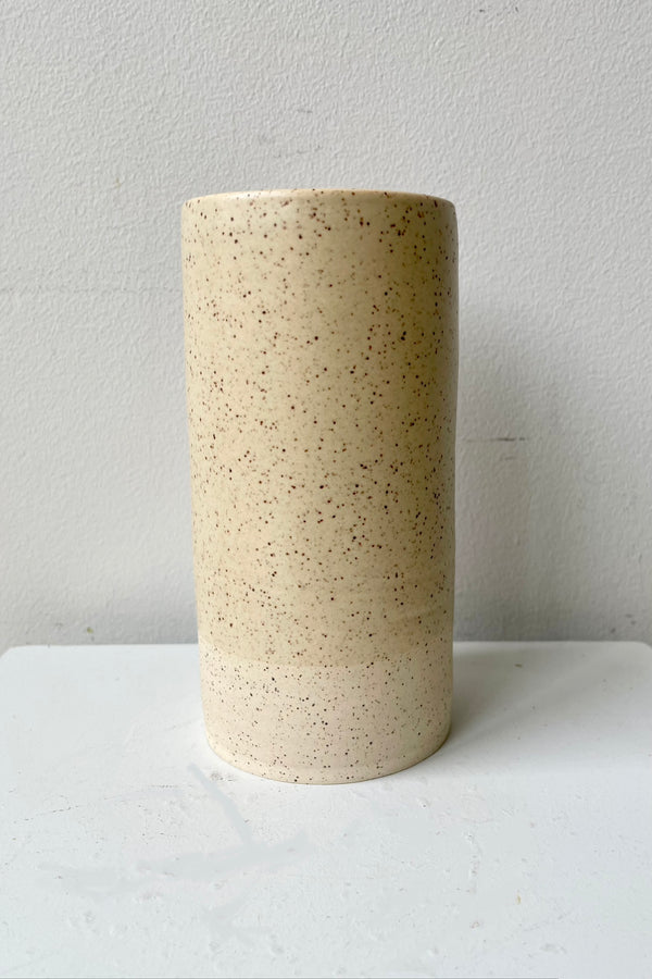 The Butter Speckle Jacqueline Vase viewed from the side against a white wall. 