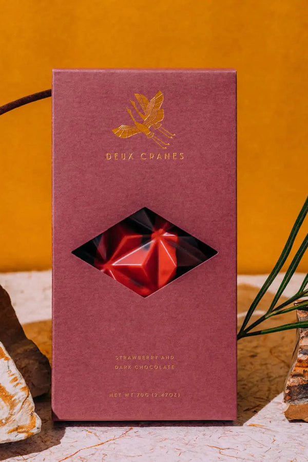 Photo of a Deux Cranes Dark Chocolate with Strawberries bar against a stone and orange background