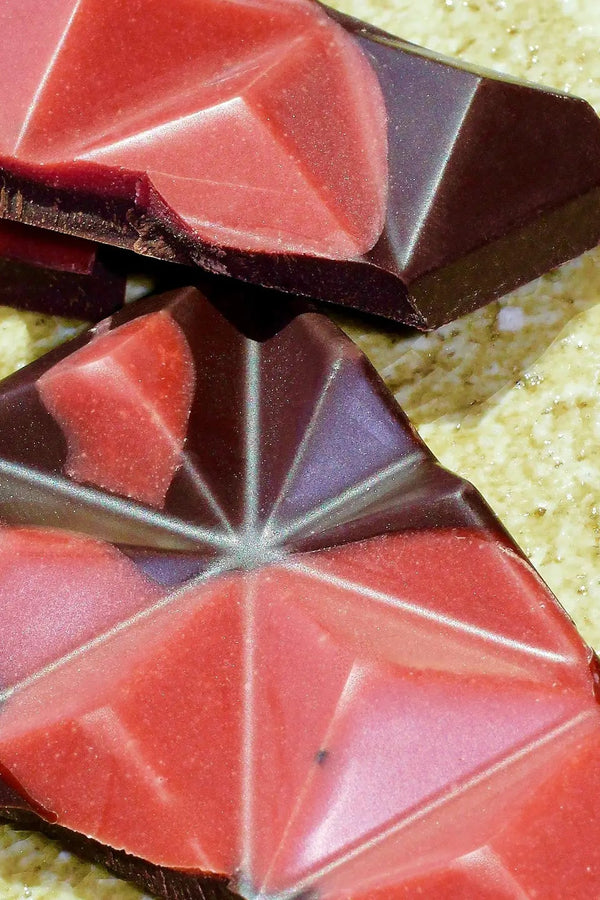 Close photo of pieces of Deux Cranes Dark Chocolate with Strawberries on a stone surface.