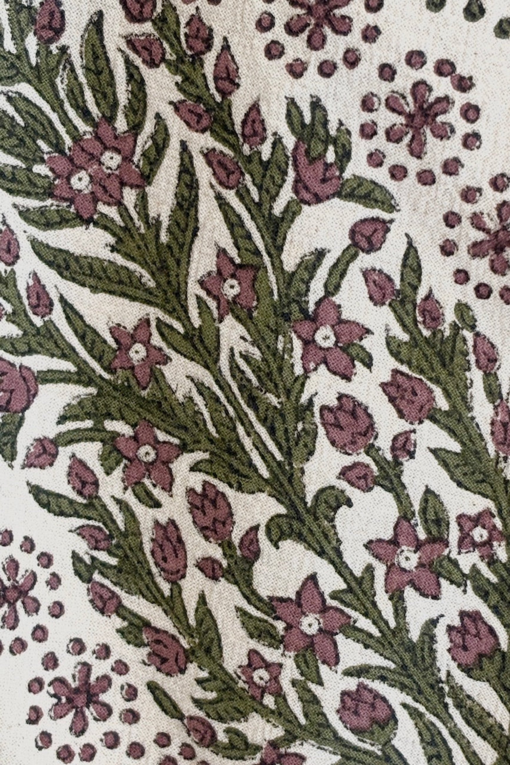 Close up of hand-block-printed napkin on Khadi cotton with a floral and dot pattern in olive and saffron colors displayed on a white surface ©Sprout Home