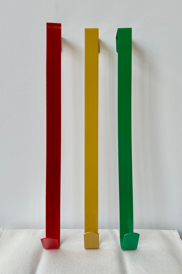 Simple wreath hanger in red, gold and green against a white wall