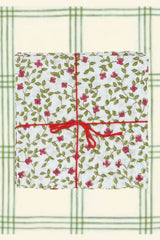 Suzette napkins Alchemille Peonie folded into squares, stacked and tied with a red string a plaid backdrop. 