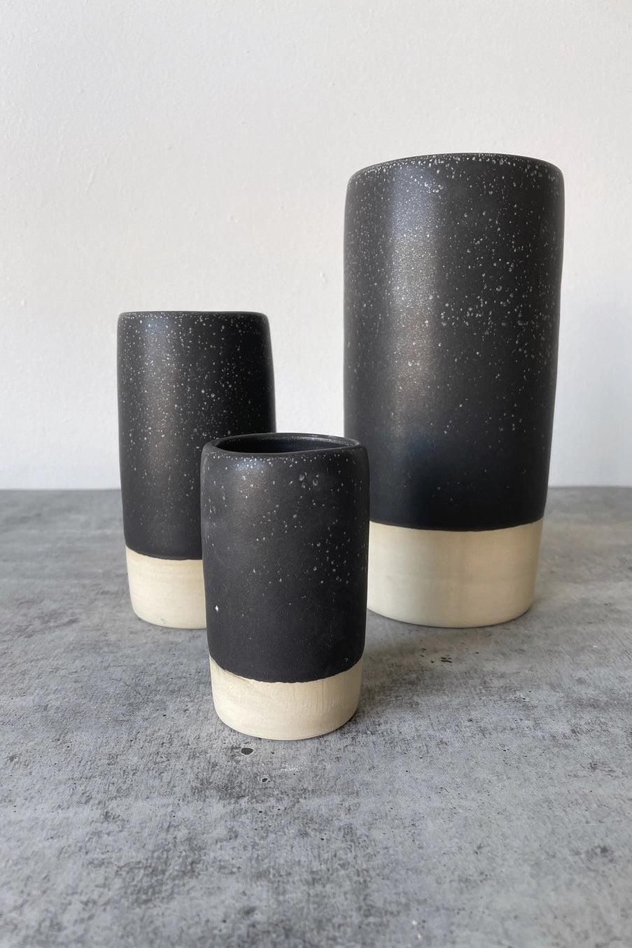 Three black ceramic Cosmos Jaqueline vases with speckled texture on a gray surface ©Little Fire Ceramics