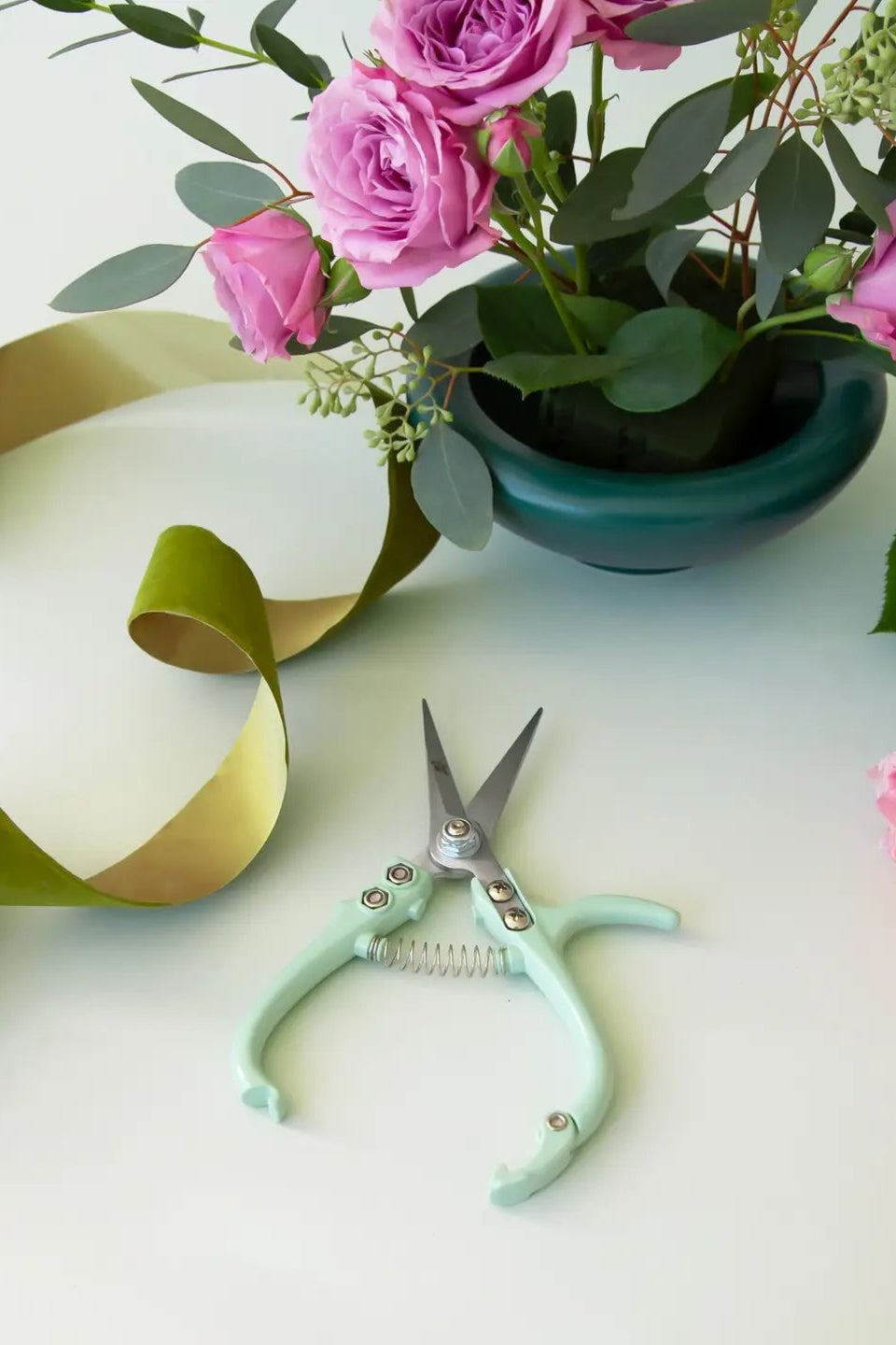 Floral arrangement with pink roses, greenery, and a pair of scissors on a light surface. ©Jungle Club