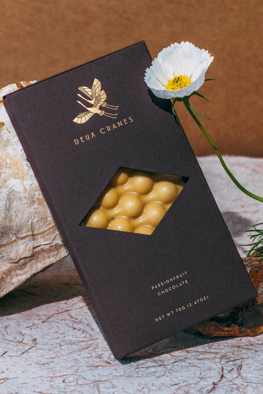 Deux Cranes passionfruit chocolate packaging with a white flower on a textured surface ©Deux Cranes