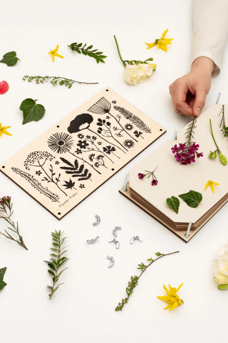 Person arranging flowers on a wooden board with floral patterns on a white background ©Studio Wald