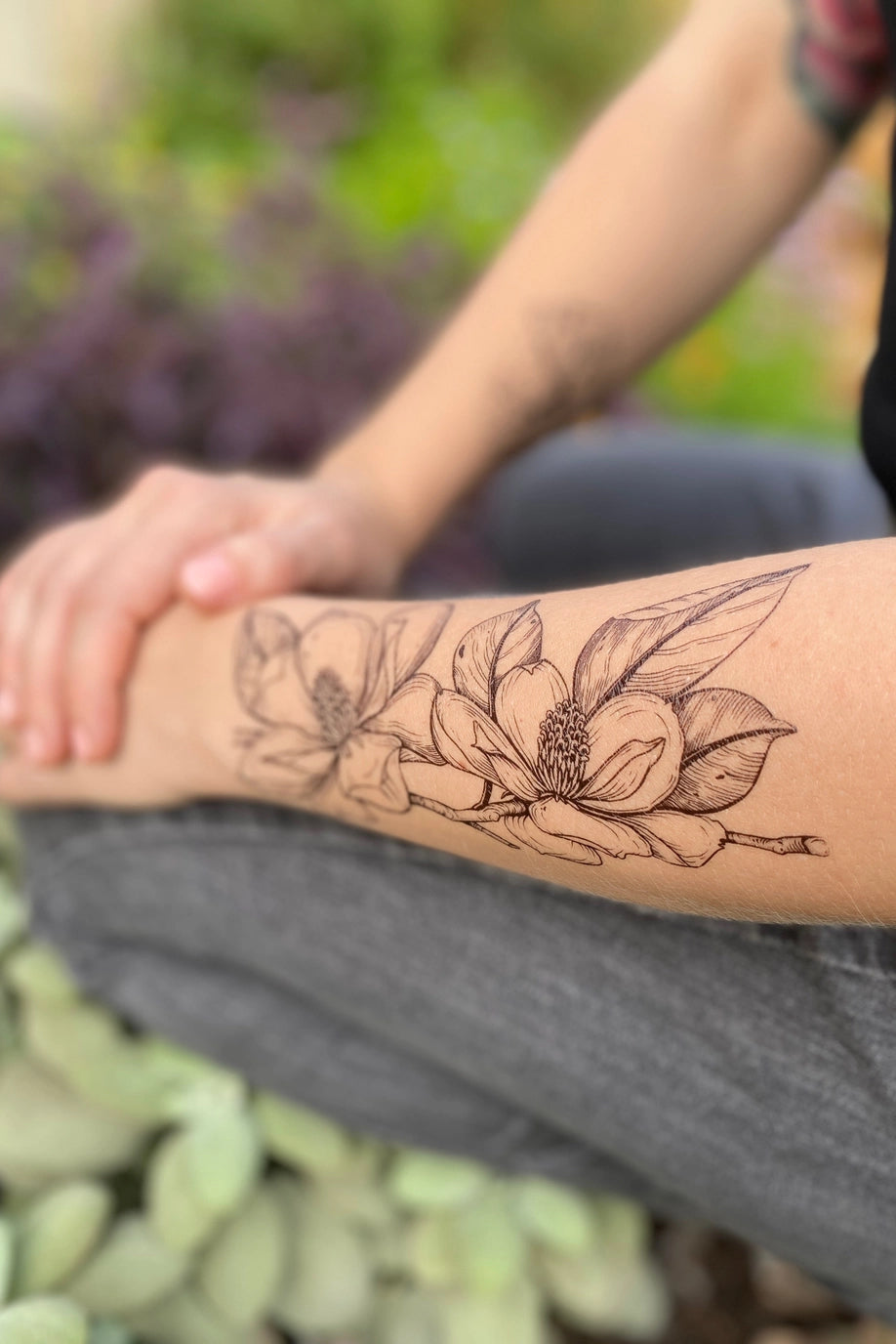 Person with a Magnolia floral tattoo on their arm sitting outdoors. ©Nature Tats