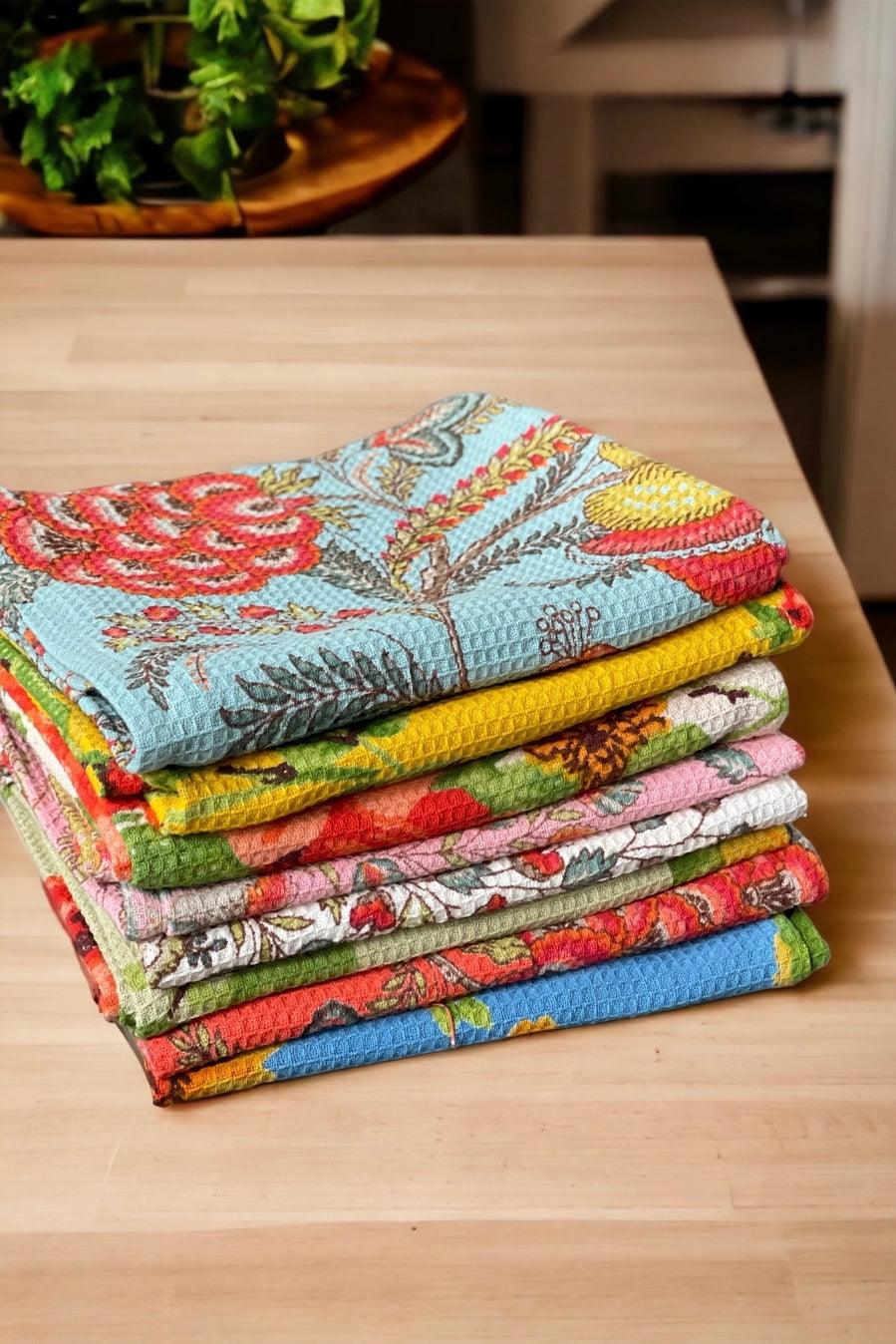 Stack of colorful fabric kitchen towels of various floral patterns on a wooden table ©Annahmol