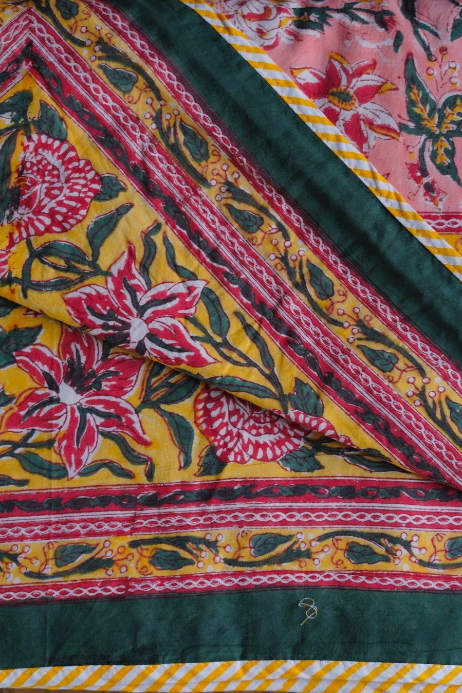 Colorful pink, yellow and green reversible blanket  fabric with floral patterns and green border ©Annahmol