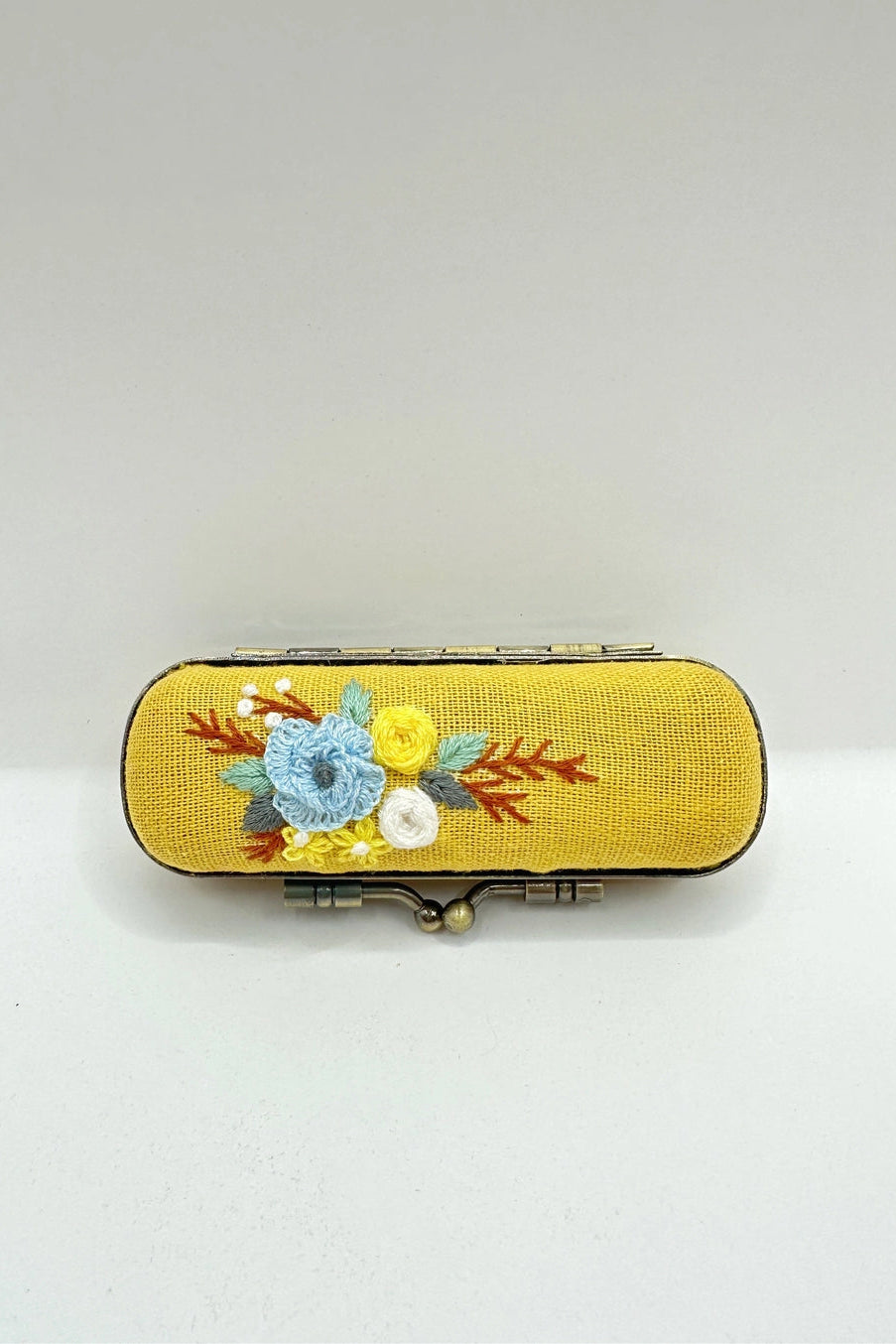 Yellow case with floral embroidery on a white background ©Quince Fables