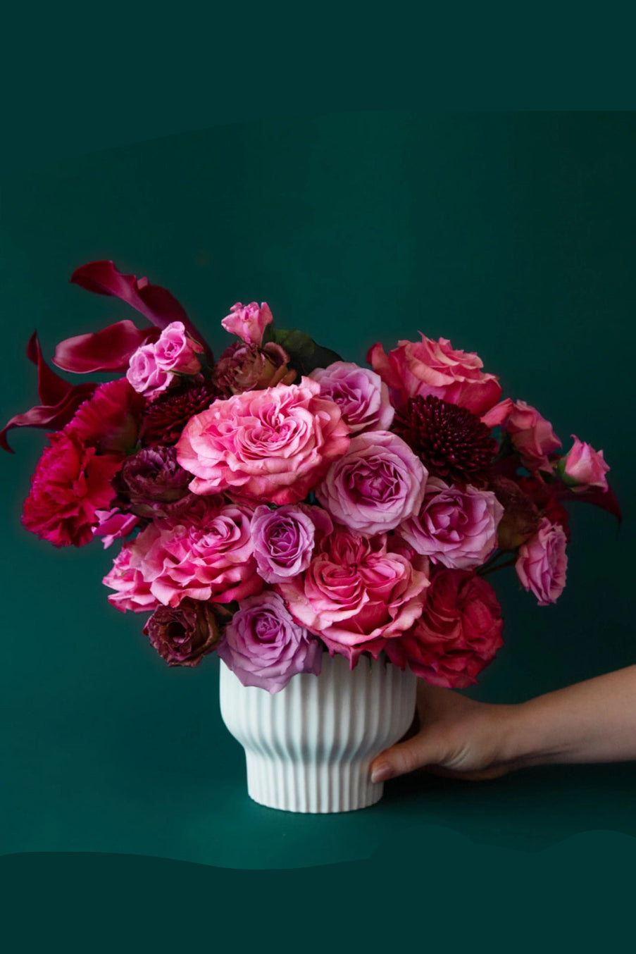 Bouquet of pink and red flowers in a white Presley vase against a dark green background ©Jungle Club