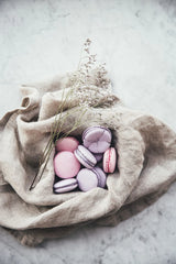 Purple and pink macaroons sitting inside a linen cloth from a page of the Flowers on a Plate book. 