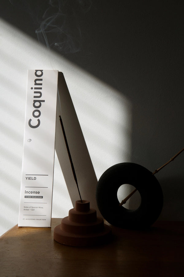 Coquina Stick Incense by Yield packaging leaning against a wall with dramatic lighting.