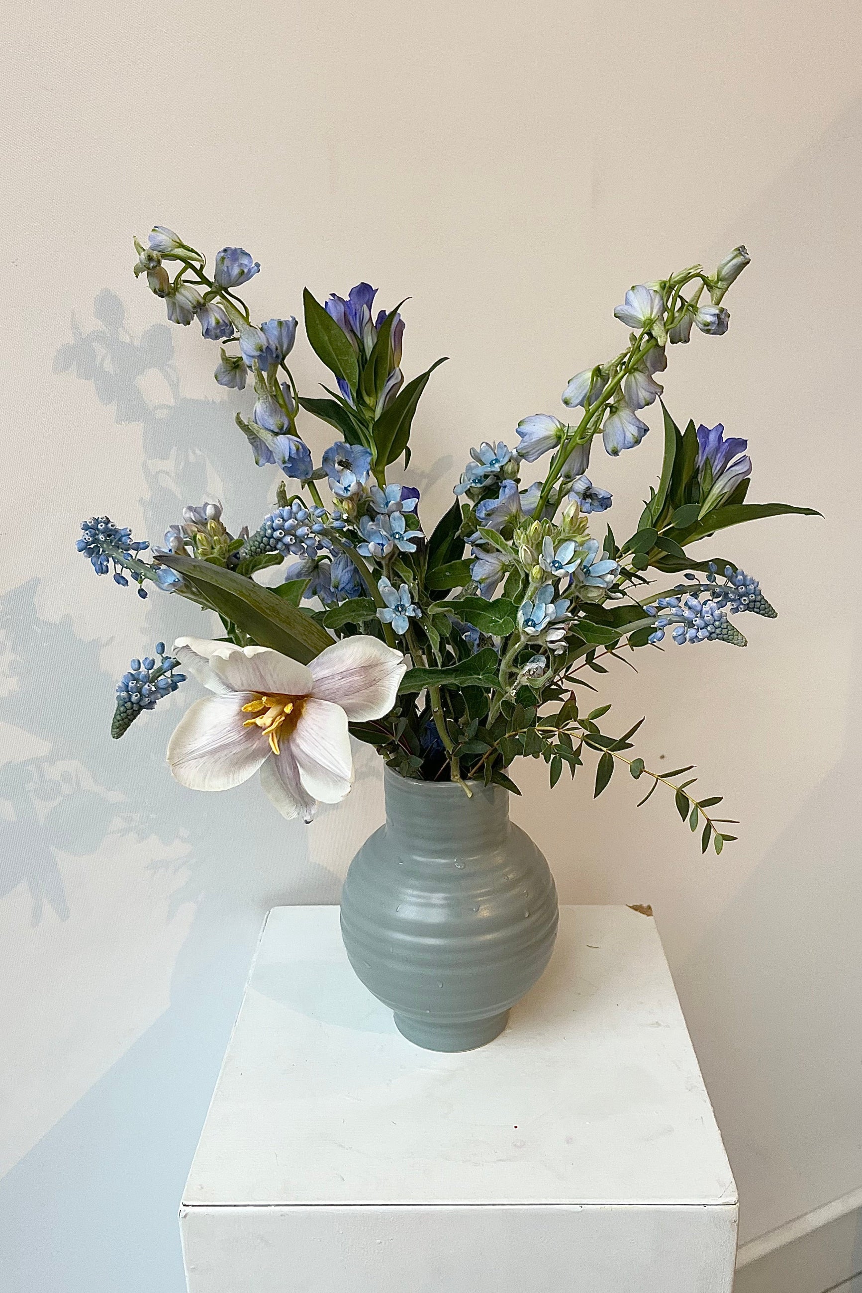 Photo of floral arrangement on a white surface in front of a white wall at Sprout Home. The flowers are various shades of blue, indigo, aqua and teal. ©Sprout Home #size_$75