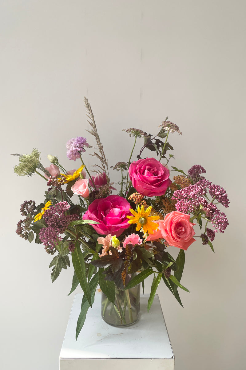 A bright mid day arrangement by Sprout Home mid June sitting against a white wall feature hot pink roses. 