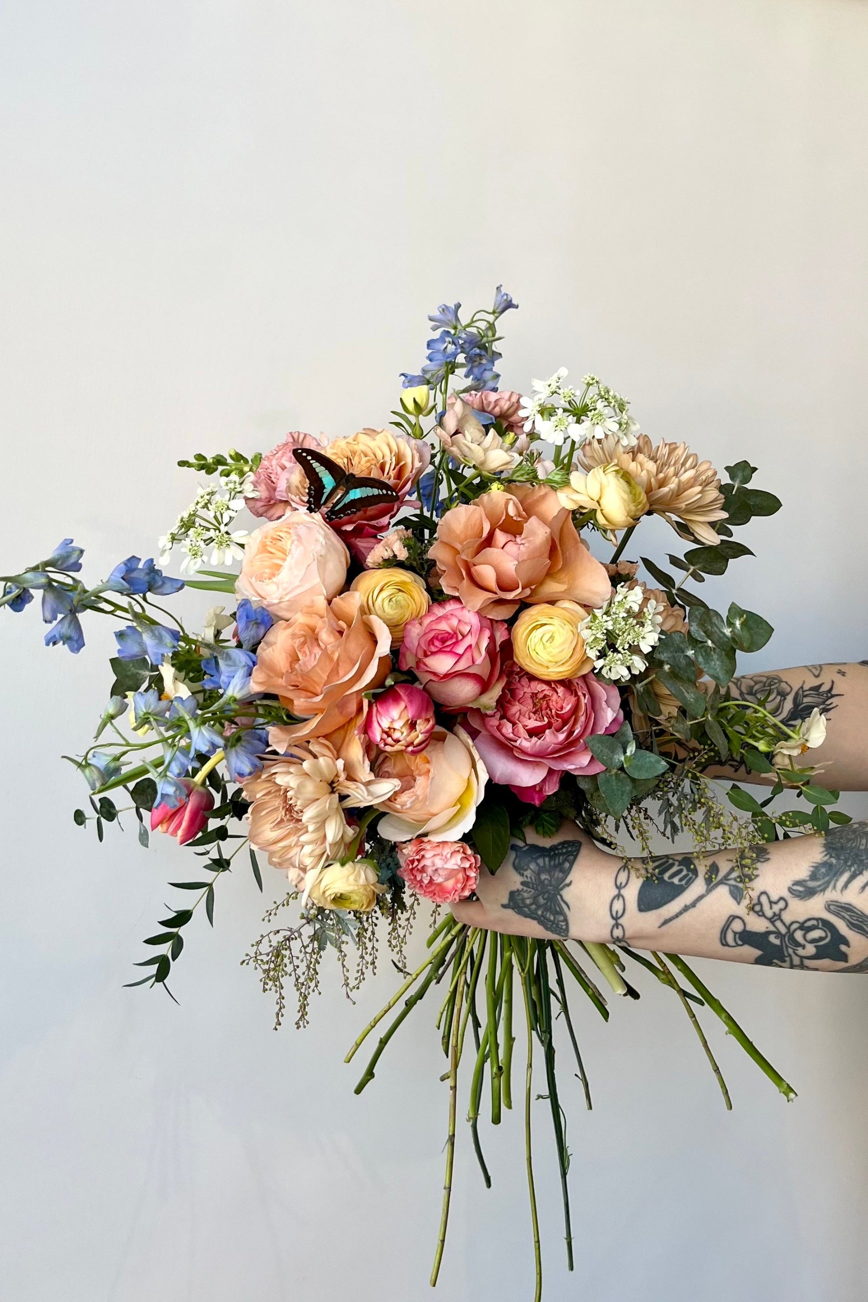 Custom floral arrangement by Sprout Home "Butterflies" with coral roses, blue delphinium and a real butterfly ©Sprout Home #size_$200