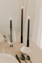 Mo & Co Charcoal beeswax taper candles shown lit and in a table setting with shades of white and cream.