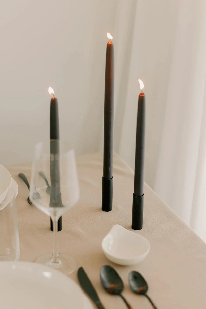 Mo & Co Charcoal beeswax taper candles shown lit and in a table setting with shades of white and cream.