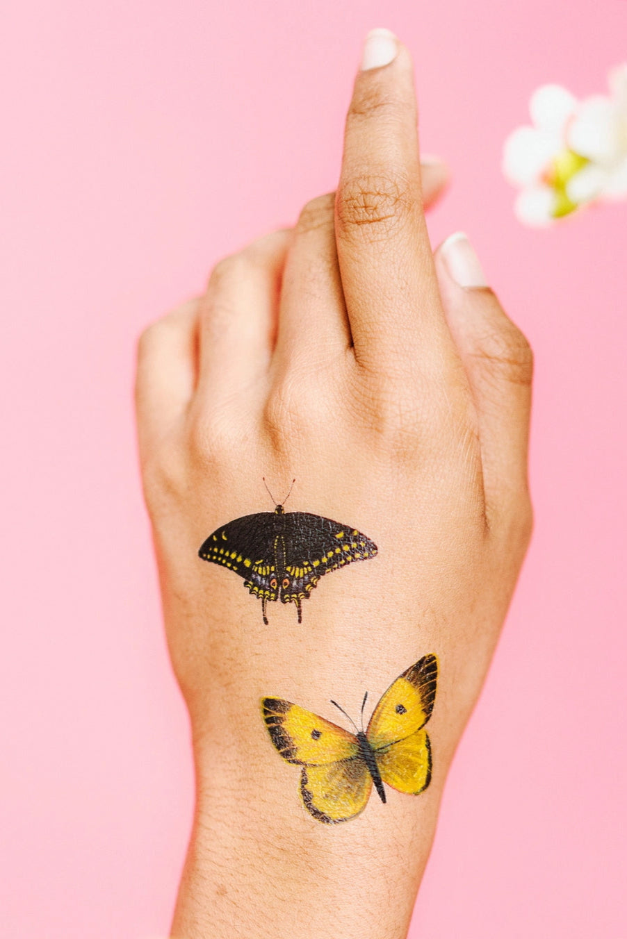 Hand with butterfly tattoos from Tiny Butterfly Tattoo Tin on a pink background ©Tattly