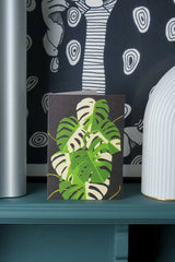 Variegated Monstera greeting card by Stengun Drawings in a lifestyle shot sitting upright in front of a white and black print.