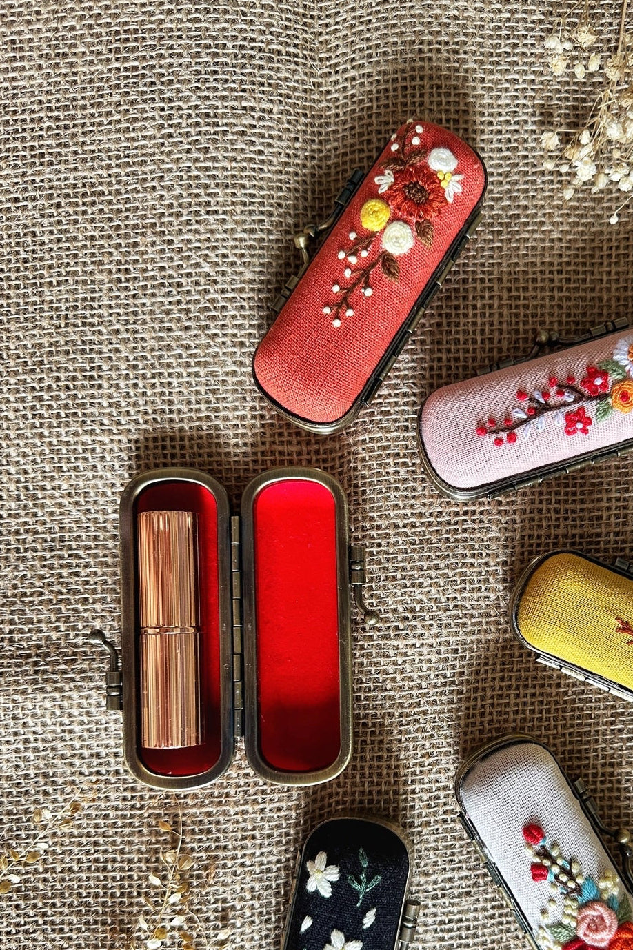 Decorative lipstick cases with floral designs on a textured fabric background ©Quince Fables