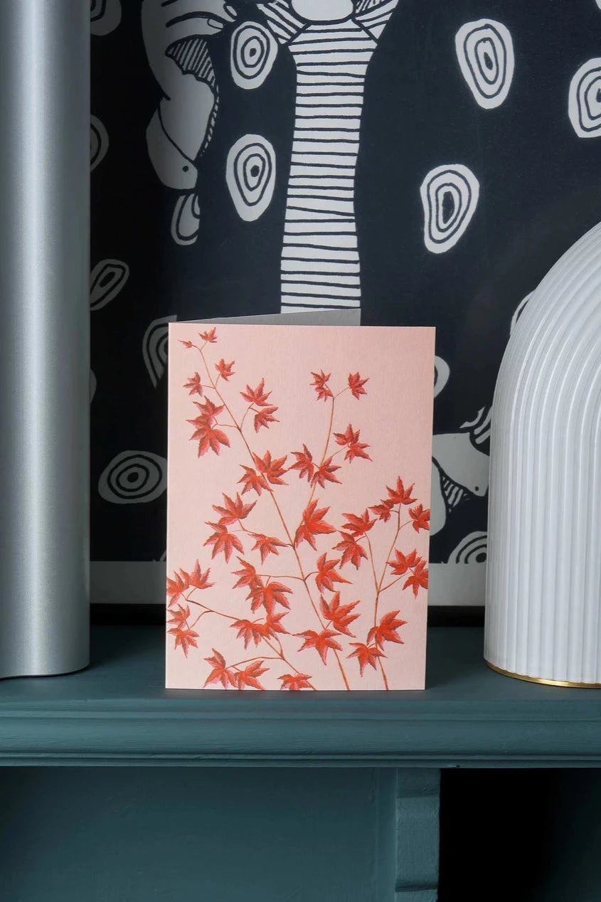 The Acer greeting card by Stengun Drawings on a shelf with a black and white wallpaper behind it. 