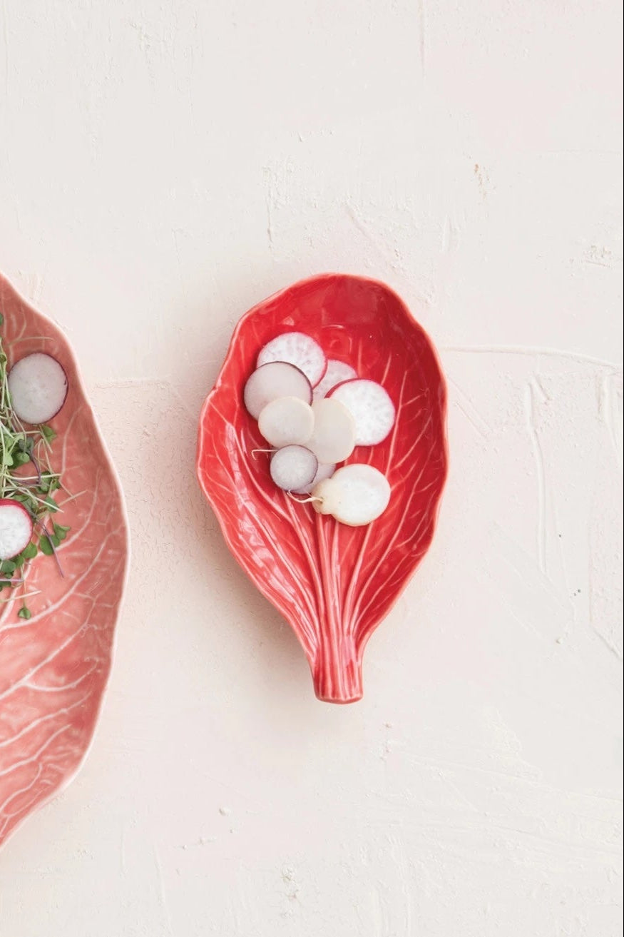 Two leaf-shaped ceramic plates with pink and red glaze holding sliced vegetables on a white surface ©Creative Co-Op)