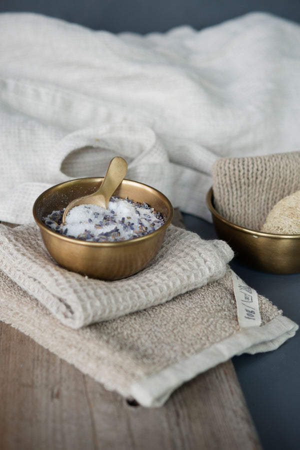 Brass bowl by Fog Linen Work in a lifestyle shot with salt inside the bowl with a metal spoon and spa linens.