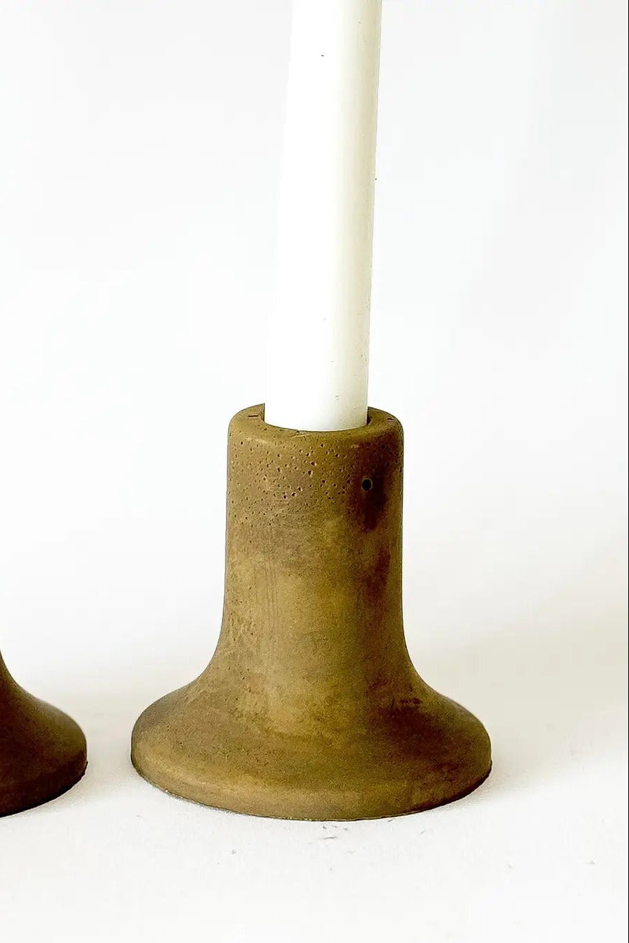 Olive concrete candle holder with white candle inserted, set against a plain white background. ©Sunday Nomad
