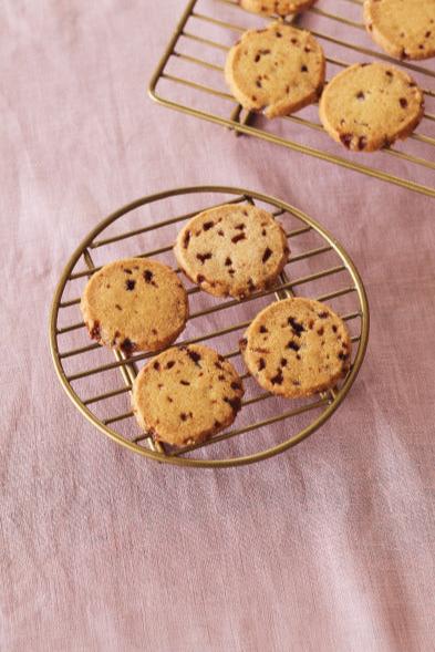 Round brass wire rack by Fog Linen Work with cookies on top of it on a pink linen table. 