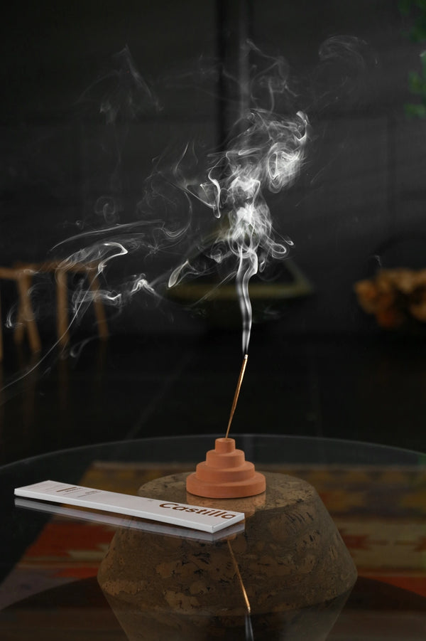 Castillo Stick Incense by Yield package on a glass table next to a burning stick showing the smoke. 