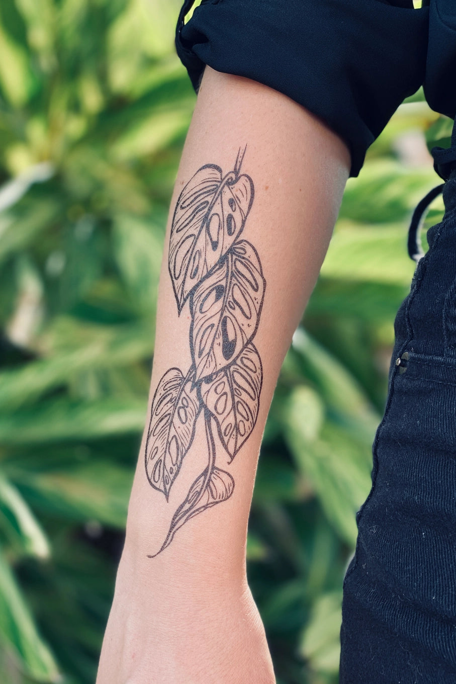 Tattoo of Monster leaf design on a person's arm with a blurred green background ©Nature Tats