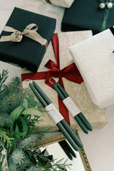 Mo & Co beeswax taper candles in Forest Green two sets being displayed on top of Christmas colored wrapped presents.