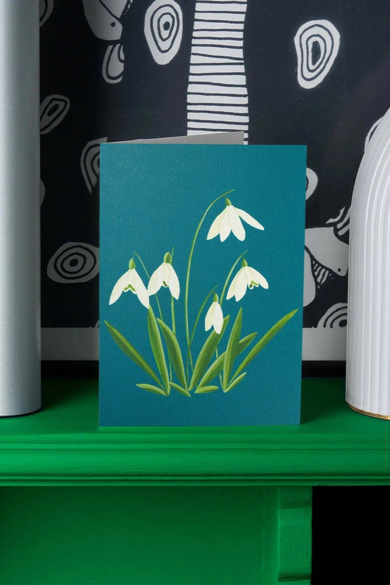 Snowdrops card by Stengun Drawings on a green shelf in front of a black a white wall paper. 