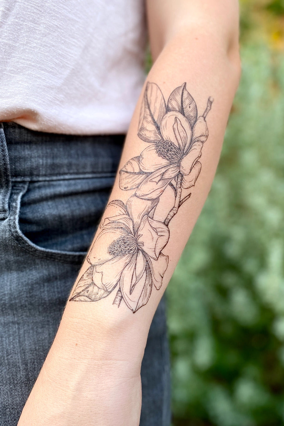 Floral Magnolia tattoo on a person's arm with a blurred green background ©Nature Tats