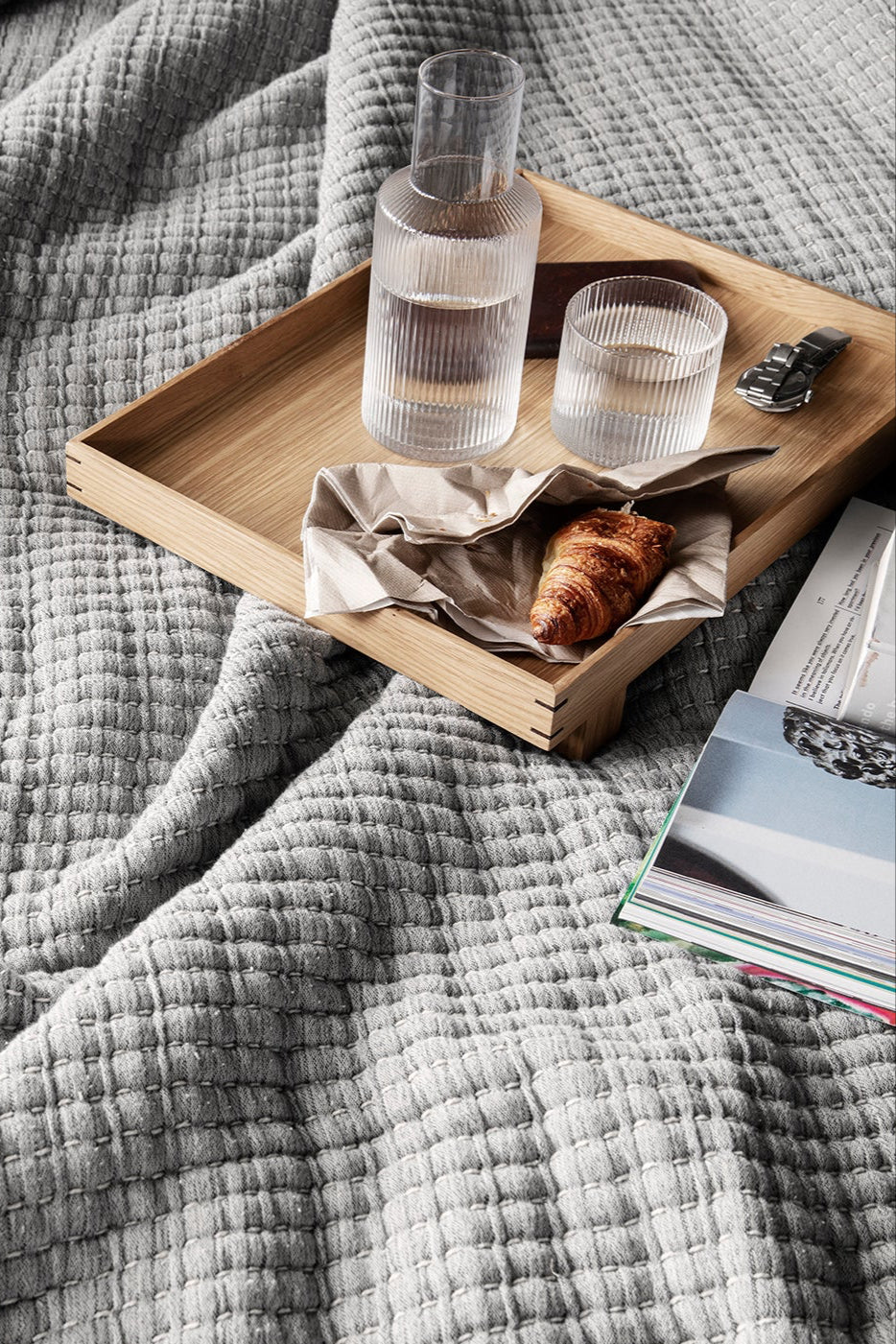 Bon Wooden Tray Oak Small shown with with a carafe, cup and croissant on a bed linen ©Ferm Living