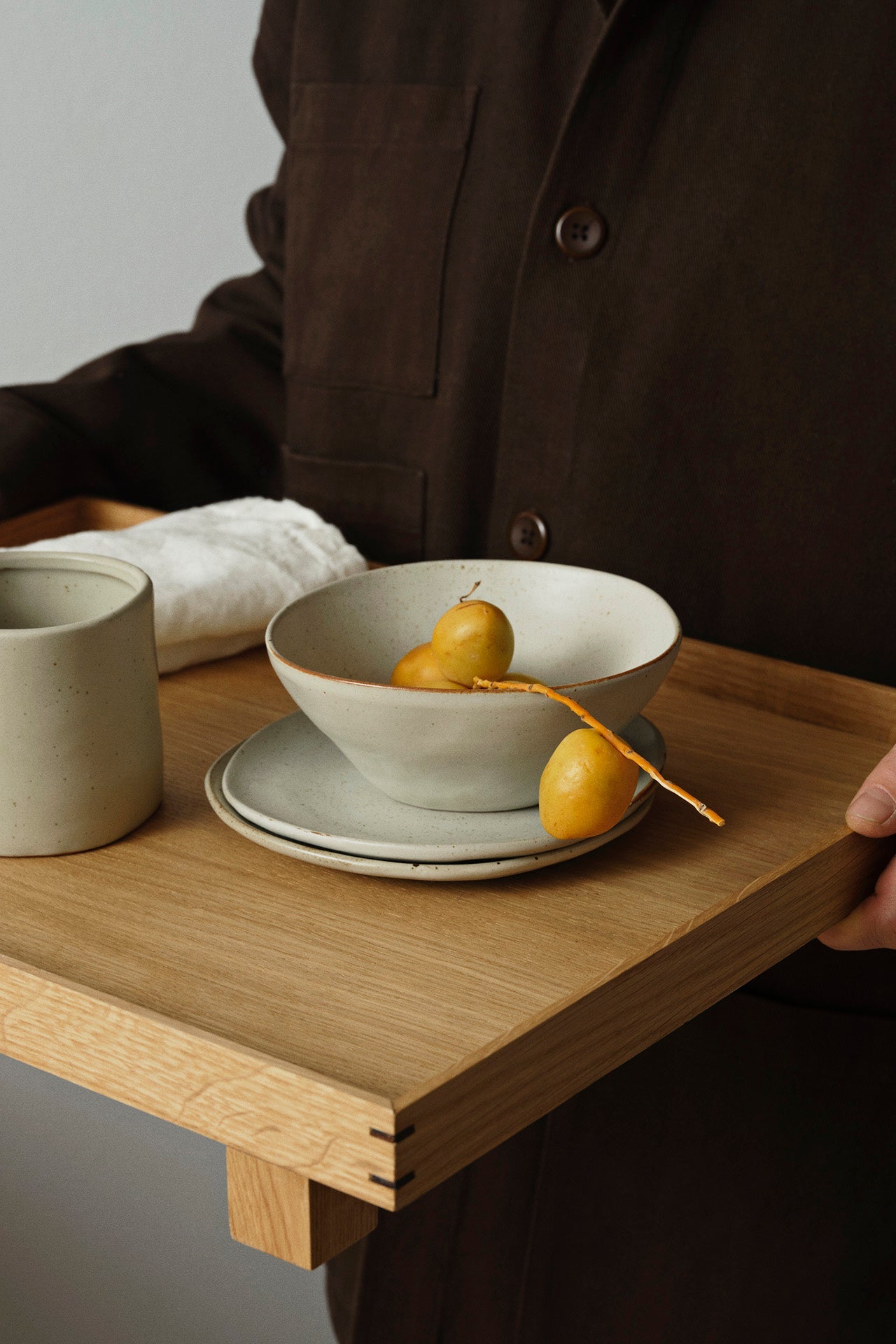 Bon Wooden Tray Oak Large in a lifestyle shot being held by a person and carryings tableware items©Ferm Living