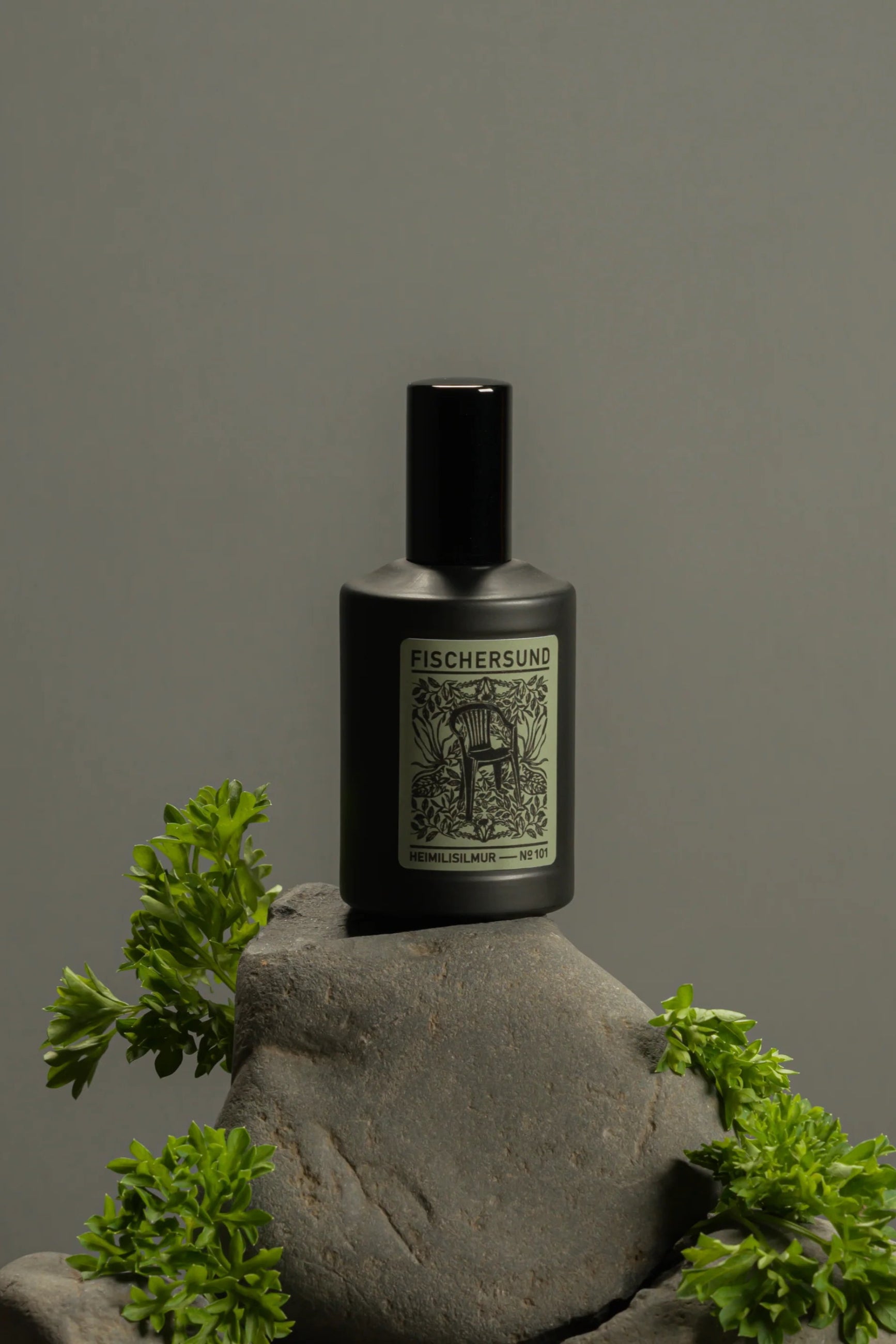Fischersund Home Spray #101 Black bottle with label on a stone surface with greenery, against a gray background ©Fischersund