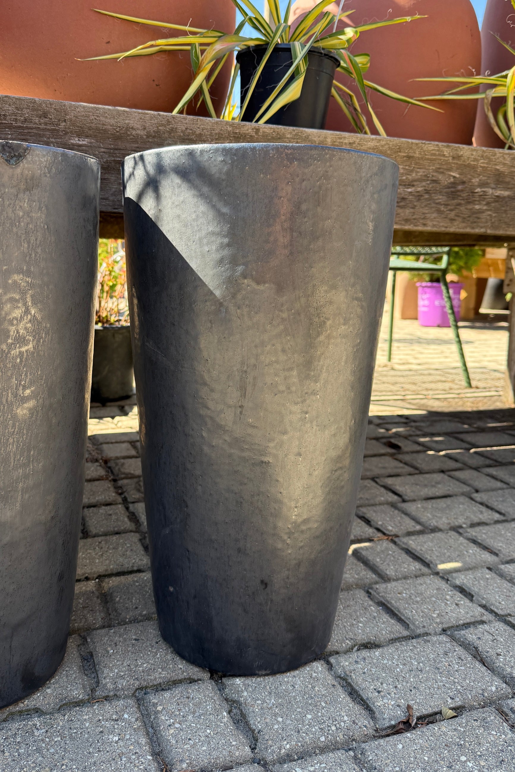 Graphite Tall Taper Planter Small on a paved surface with plants in the background. ©Sprout Home