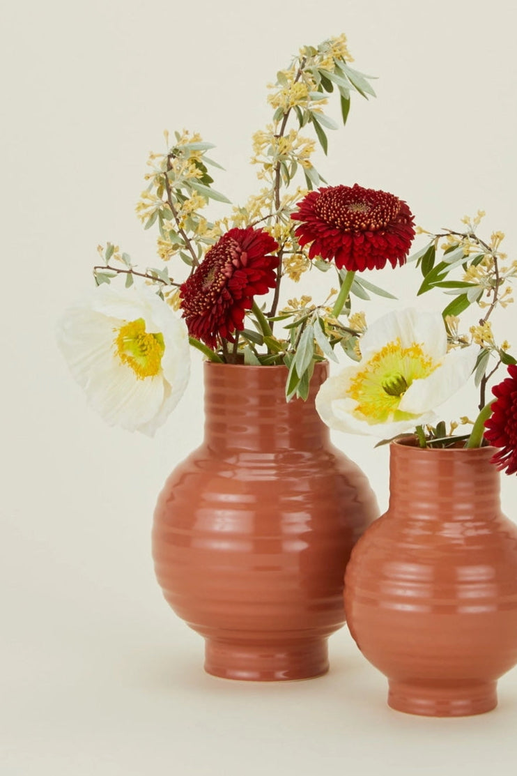 Terracotta-colored Hawkins New York Essential vases with flowers in them,  on a beige background ©Hawkins New York